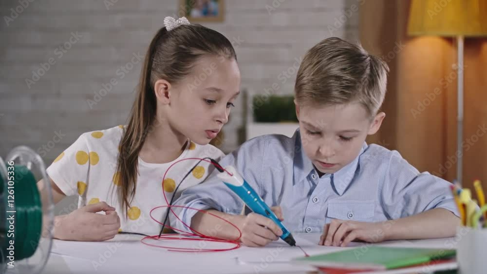 Girl talking something to her friend using 3d pen to make drawing on paper Girl talking something to her friend using 3d pen to make drawing on paper