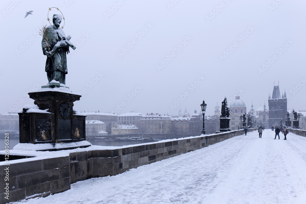 Snowy foggy Prague Old Town with Bridge Tower and St. Francis of Assisi Cathedral from Charles Bridge with its baroque Statues, Czech republic