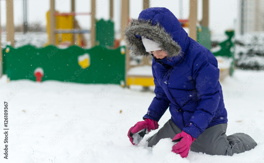 Little girl rolling snowball in winter.