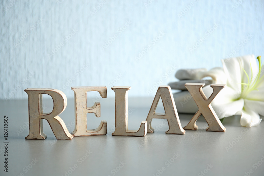 Word RELAX made of wooden letters with spa stones and flower on table Word RELAX made of wooden letters with spa stones and flower on table