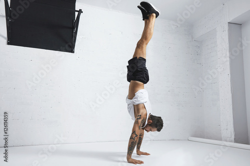 Fotografie Strong tattooed in white unlabeled tank t-shirt male athlete shows calisthenic m