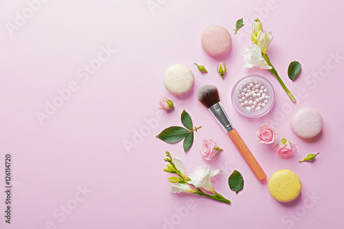 Mineral powder with brush, macaroons and beautiful flowers on pink background