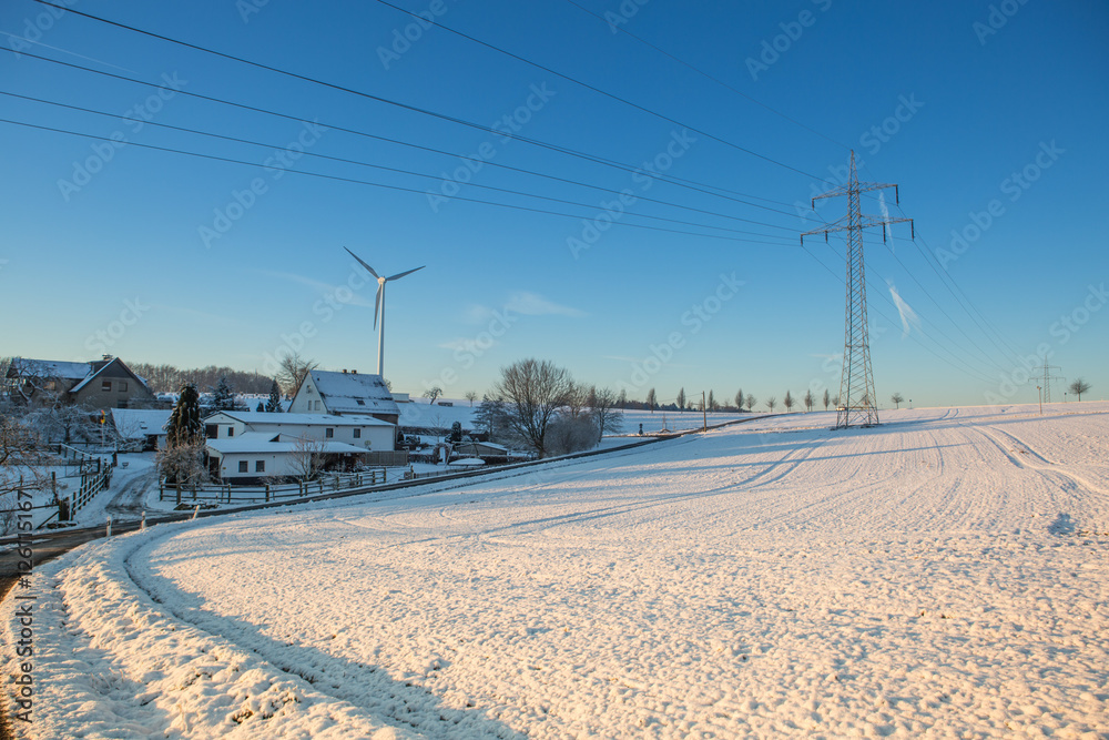 Winterlandschaft mit Oberleitungen für Strom im Gegenlicht bei blauem Himmel