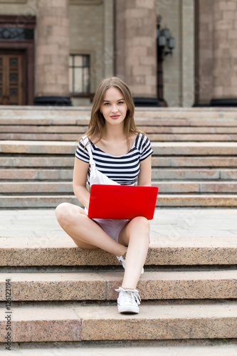 Young beautiful woman with laptop sitting on stairs near the university