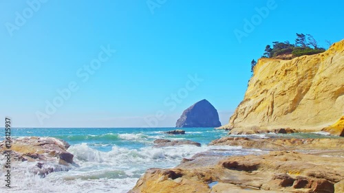 Cinematic, sliding shot of iconic Cape Kiwanda beach in Oregon by Pacific Coast Highway, scenic landscape. Spectacular coastal of a rock formations with blue water and breaking waves on a sunny day