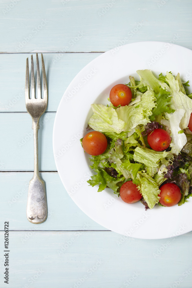 Aerial view of a dish of classic side salad with fork, on a blue wooden table top background Aerial view of a dish of classic side salad with fork, on a blue wooden table top background