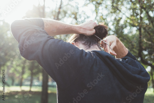 Back view of young man in backlight gathering his hair in pigtail - hair care, hair style concept