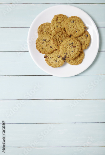 Aerial view of a plate full of freshly baked oatmeal and raisin cookies on a blue wooden table background with blank space below