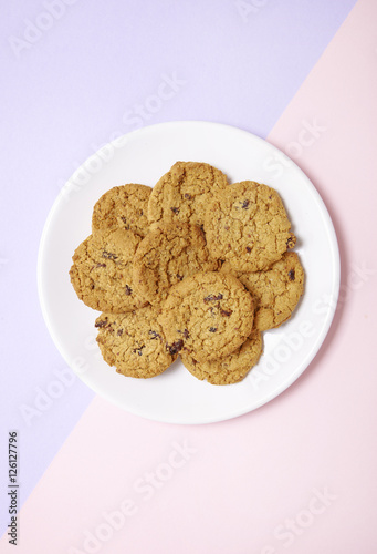 Overhead view of a plate full of freshly baked oatmeal and raisin cookies on a pastel pink and purple background