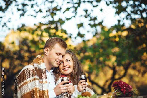 Loving couple with wine glasses embracing at the autumn park.
