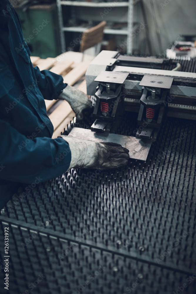 Manual worker doing some steel cutting job in factory for production boiler stoves. Dark conditions. Selective focus. Low light.