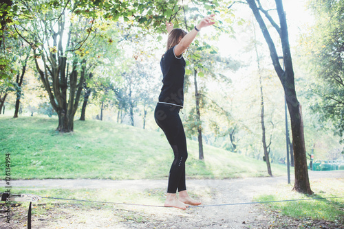 Woman balancing a tightrope or slackline outdoor in a city park in autumn - slacklining, balance, training concept