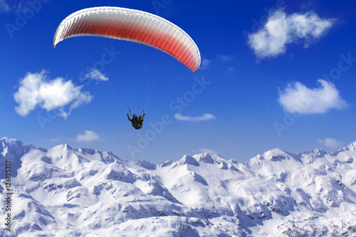 Paragliding over the mountains on background of blue sky and whi