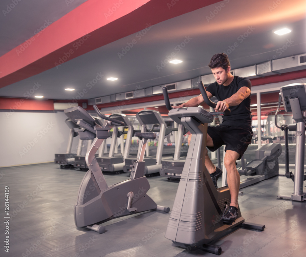 Fototapeta premium young man exercise bike, cycling, stationary exercising.