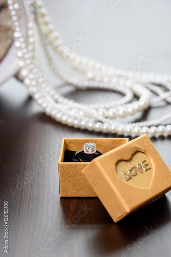 Diamond ring in the box on wooden table. Opened gift jewelry box. Box with the name of "love". Pearls in the background. Place for text, copyspace.