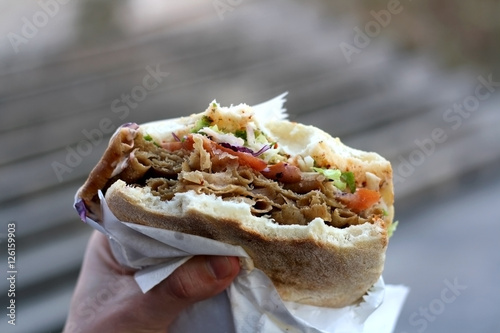 Doner kebab stuffed into a pita with tomatoes, cabbage and lettuce. Eating outdoor. Selective focus. 
