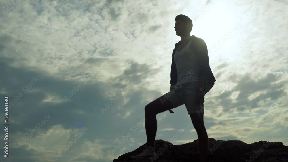 Young tall man wearing fashionable summer clothes staying on the top of a stone and watching the beauty of the sea. Young tall man wearing fashionable summer clothes staying on the top of a stone and watching the beauty of the sea.