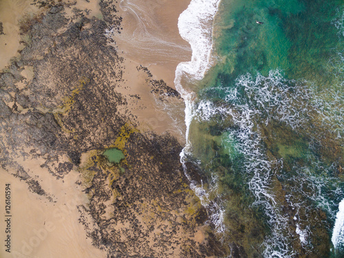 Birds eye view of the tide and surfer coming in at a surf beach