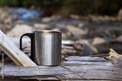 Metal travel mug stands on a log on the background of a mountain