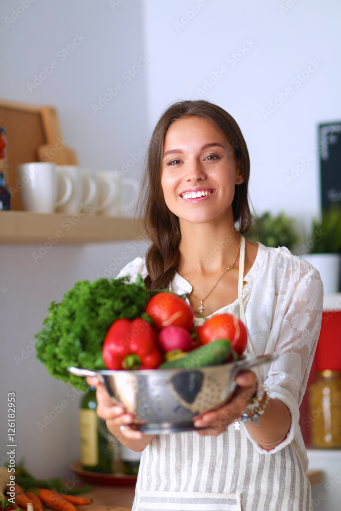 Smiling young woman holding vegetables standing in kitchen Smiling young woman holding vegetables standing in kitchen