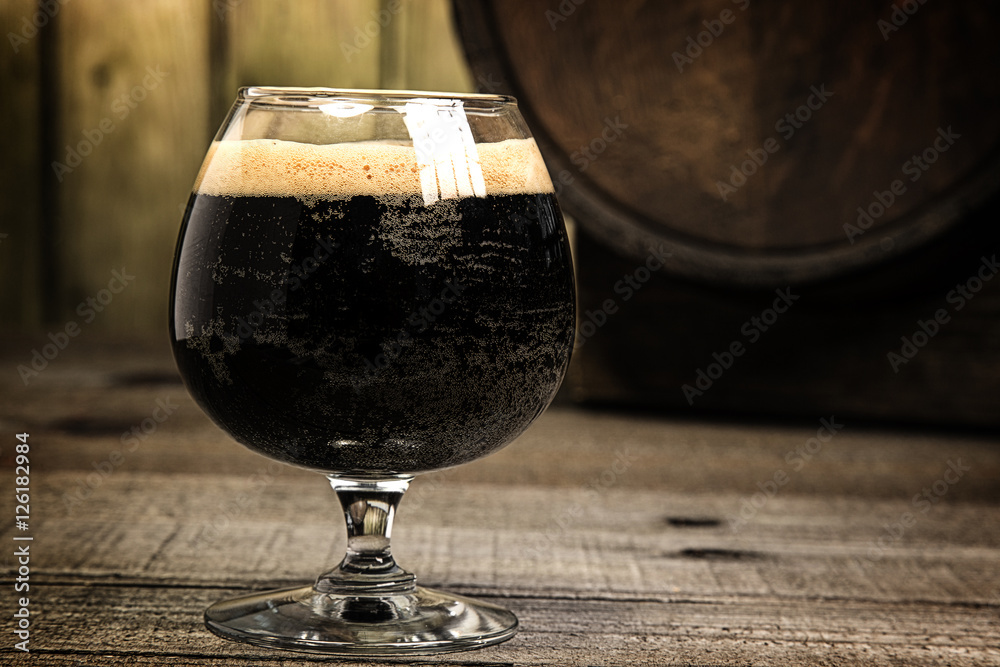 Russian Imperial Stout in snifter glass on wood background and b - obrazy, fototapety, plakaty 
