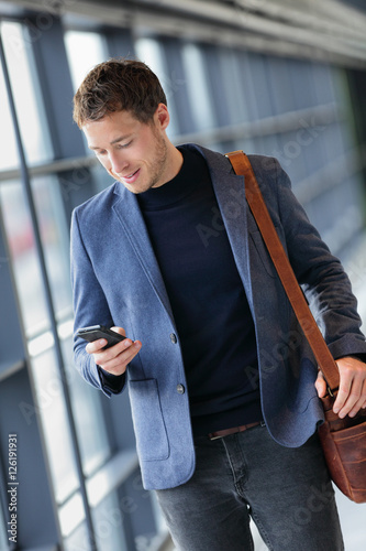 Man on smart phone - young business man texting in airport. Casual urban professional businessman using smartphone app smiling happy inside office building or airport.