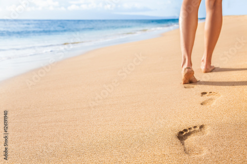 Beach travel - woman relaxing walking on sand beach leaving footprints in the sand. Closeup detail of female feet and legs on golden sand on Kaanapali beach, Maui, Hawaii, USA. photo