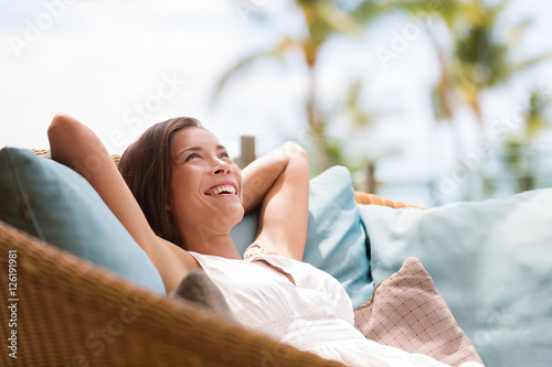 Home lifestyle woman relaxing enjoying luxury sofa patio furniture on outdoor patio living room. Happy lady lying down on comfortable pillows daydreaming thinking. Beautiful young Asian chinese girl. photo