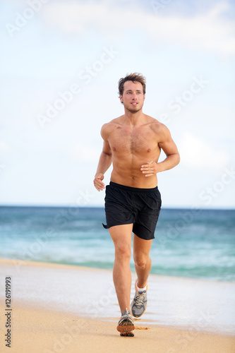 Beach fitness man runner running training cardio. Healthy lifestyle male athlete doing exercise living an active life working out on sunset beach with ocean background topless in shorts. © Maridav