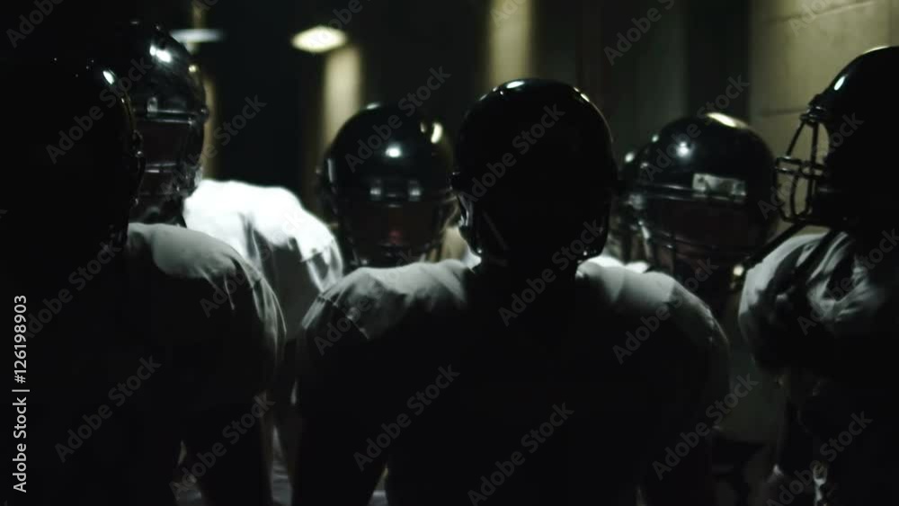 Football team walks down a dark tunnel towards the field before a game