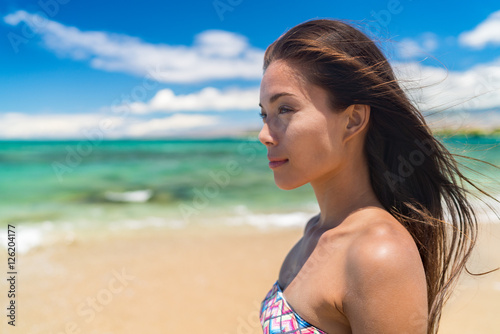Beautiful serene asian beauty portrait of woman relaxing on tropical beach with turquoise ocean water background. Relaxation getaway in the sun, gorgeous chinese model in swimwear and healthy hair.