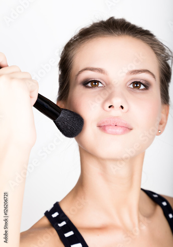 Close-up Female model applying makeup on her face. Beautiful young woman applying foundation on her face with a make up brush.
