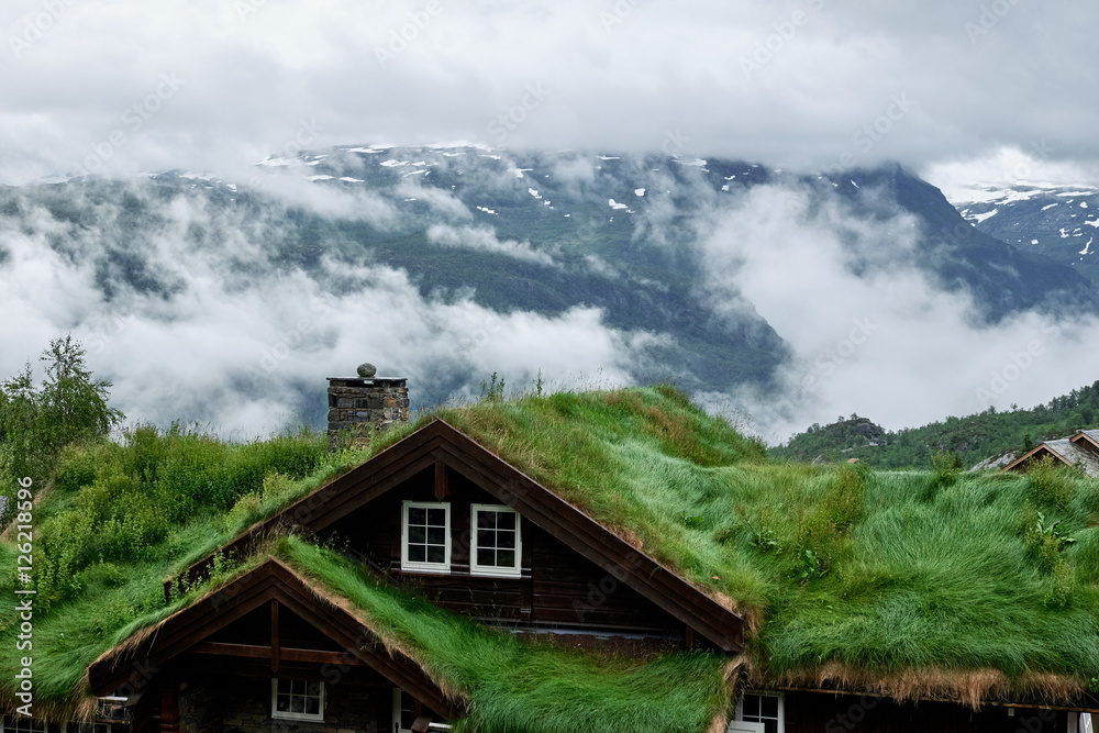 The roof of a Norwegian cottage covered with grass, in front of a mountain top hidden in low hanging clouds