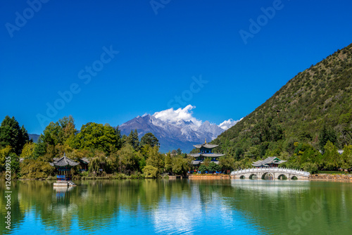 Black Dragon Pool to the Five Phoenix Tower and the Five Holes Bridge. In the background is Jade Dragon Snow Mountain. The Old Town of Lijiang is located in Lijiang City, Yunnan, China.
