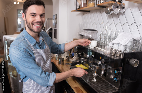 Joyful handsome waiter using coffee machine.