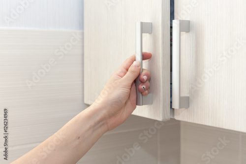 Billede på lærred Female hand open the cupboard doors, close up