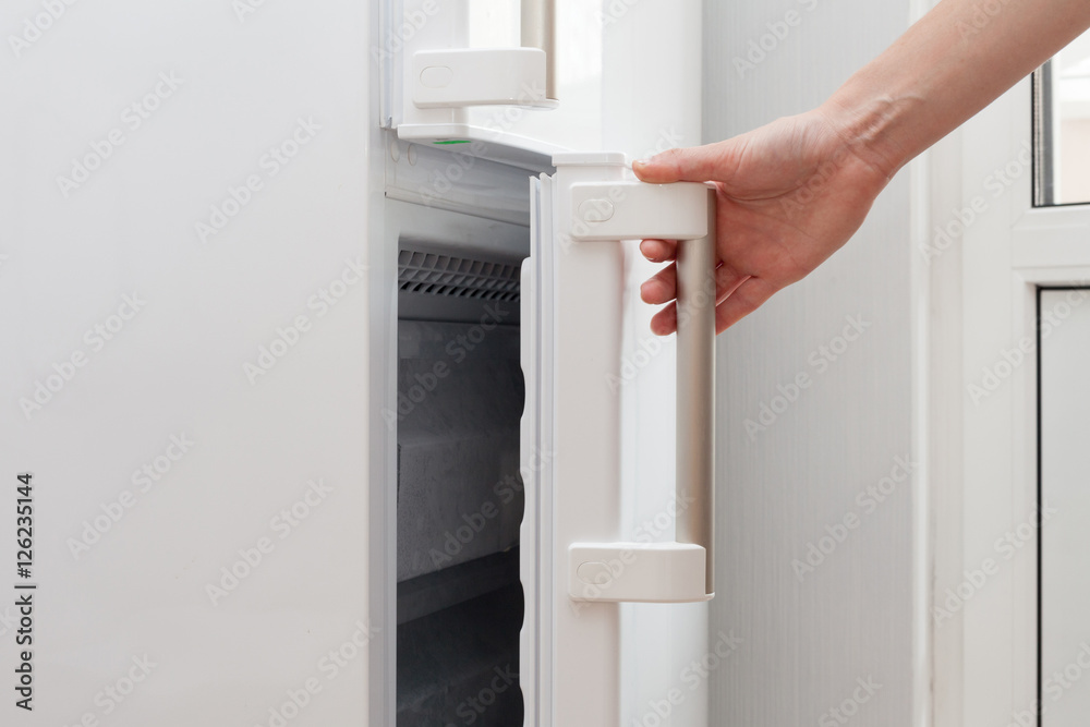 The hand of a young man is opening a freezer door The hand of a young man is opening a freezer door