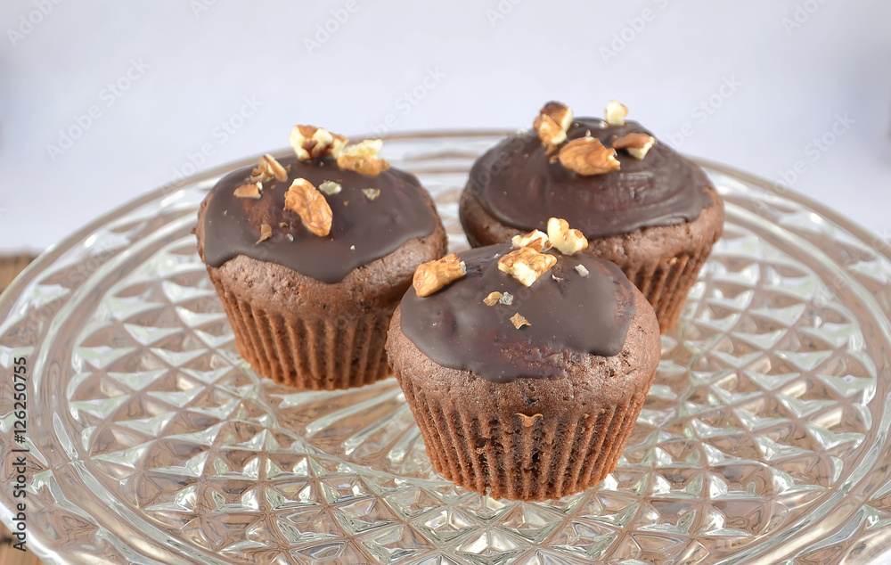 three chocolate brown muffins with nuts on glass tray