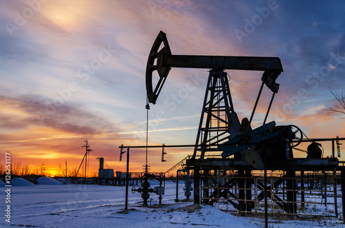 Oil pump, wellhead, pipeline silhouette during sunset at the oilfield. Winter time. Oil and gas concept. 