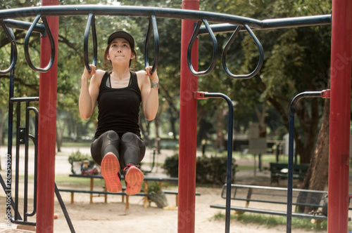 Young fit woman doing a pull up workout at a playground. 