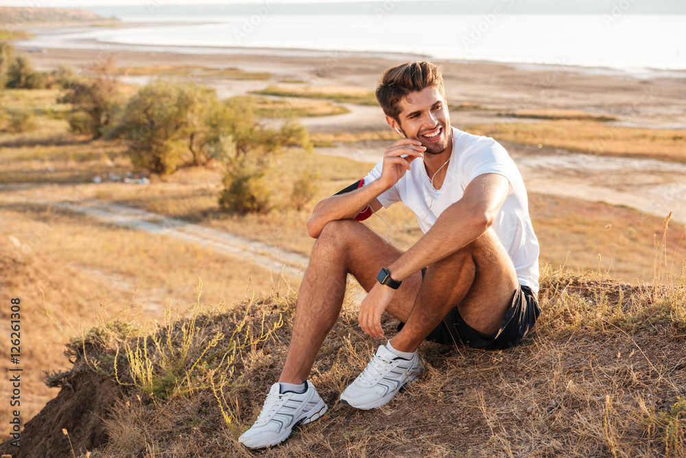 Φωτογραφία Young sportsman resting and listening music with earphones after workout