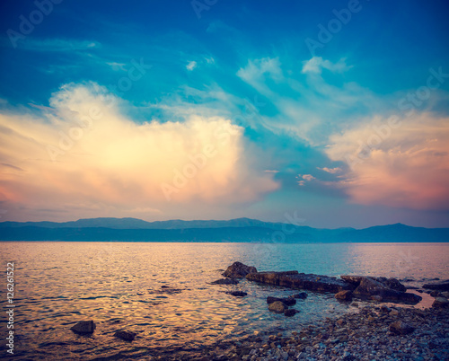Beautiful Sea with Blue Sky and White Clouds at Sunset. Pebble Beach in Croatia  Europe. Evening Seascape in Dalmatia  Adriatic Sea. Coastline and Mountains on the Horizon. Toned and Filtered Photo.