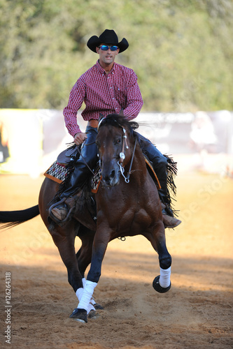 The front view of a rider in cowboy chaps, boots and hat on a horseback performs an exercise during a competition