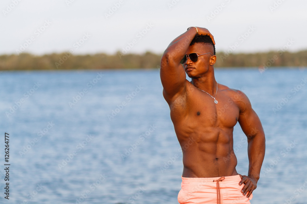 Fotografia do Stock: Muscular young athletic sexy man on the beach with a  naked torso in underwear. Hot black beautiful guy, fitness model with a  rangy sports body.