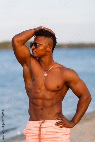 Muscular young athletic sexy man on the beach with a naked torso in underwear. Hot black beautiful guy, fitness model with a rangy sports body.