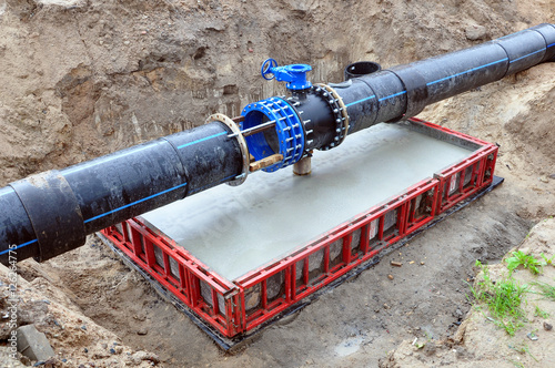 The process of installation of the distribution unit heating network. Frame for connecting pipes on a concrete support in the trench of sand. photo