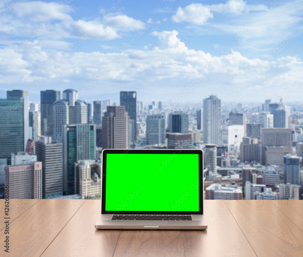 Blank green screen laptop computer on wooden table with cityscap Blank green screen laptop computer on wooden table with cityscap