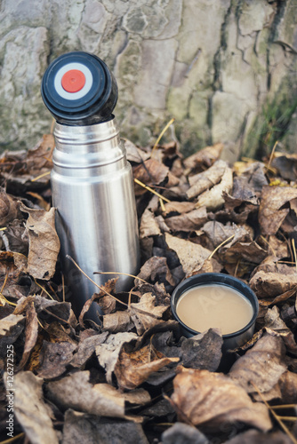 Thermos with coffee in fallen leaves