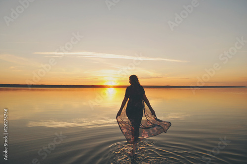 Силуэт женщины, которая идет по воде на закате солнца