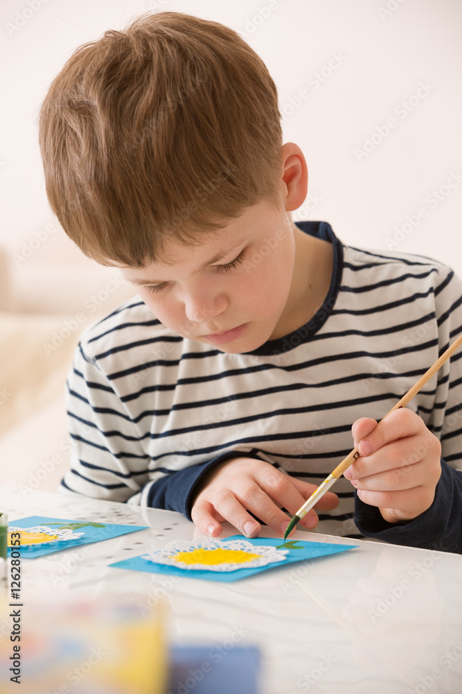 Portrait of little school boy sitting at the table and drawing with yellow paint. After school activities at home. Education. Small boy creating handmade cards. Portrait of little school boy sitting at the table and drawing with yellow paint. After school activities at home. Education. Small boy creating handmade cards.